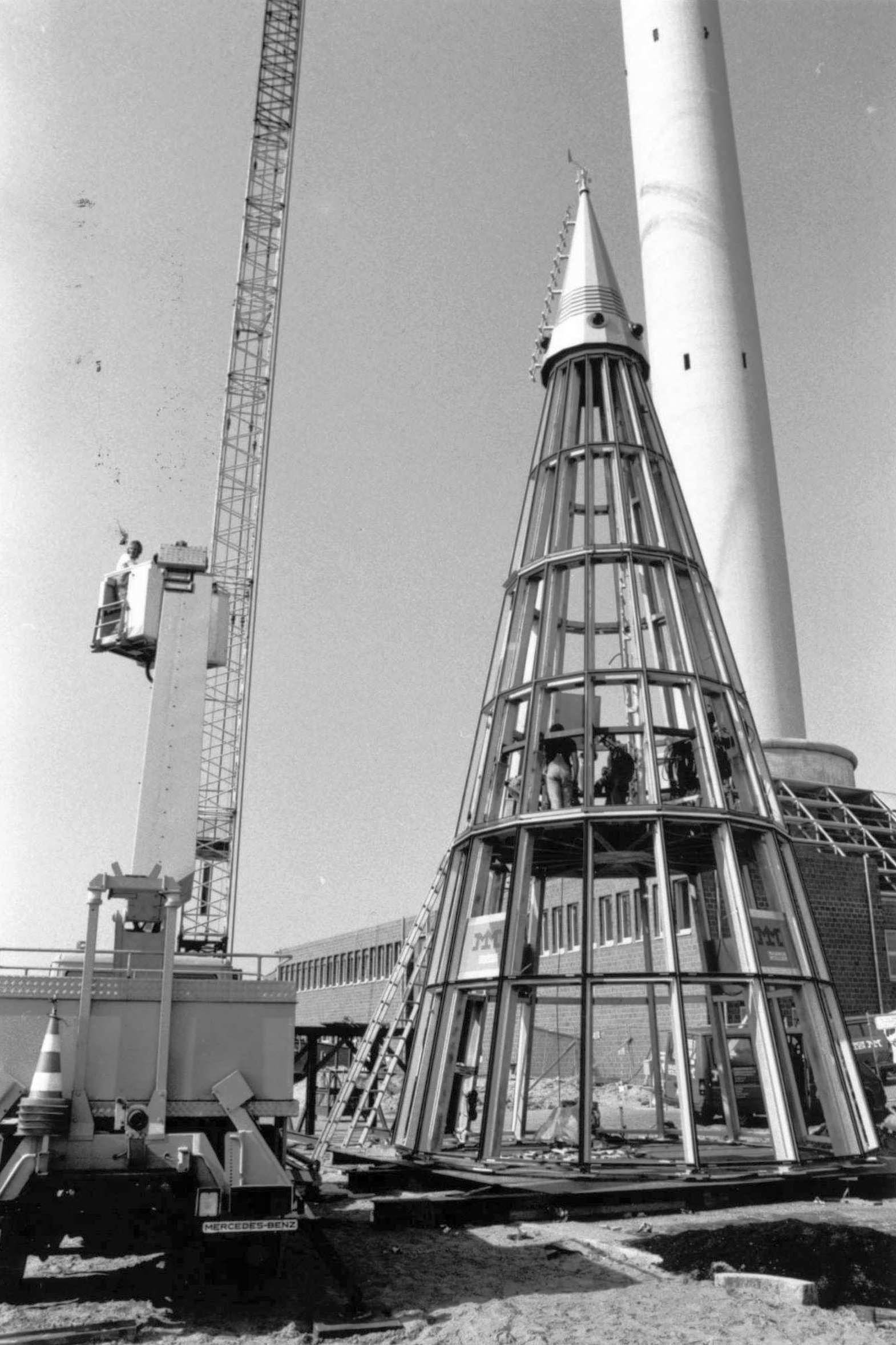 Vier Fotos zeigen die schrittweise Montage der kegelförmigen Spitze auf dem Fallturm im August 1989.