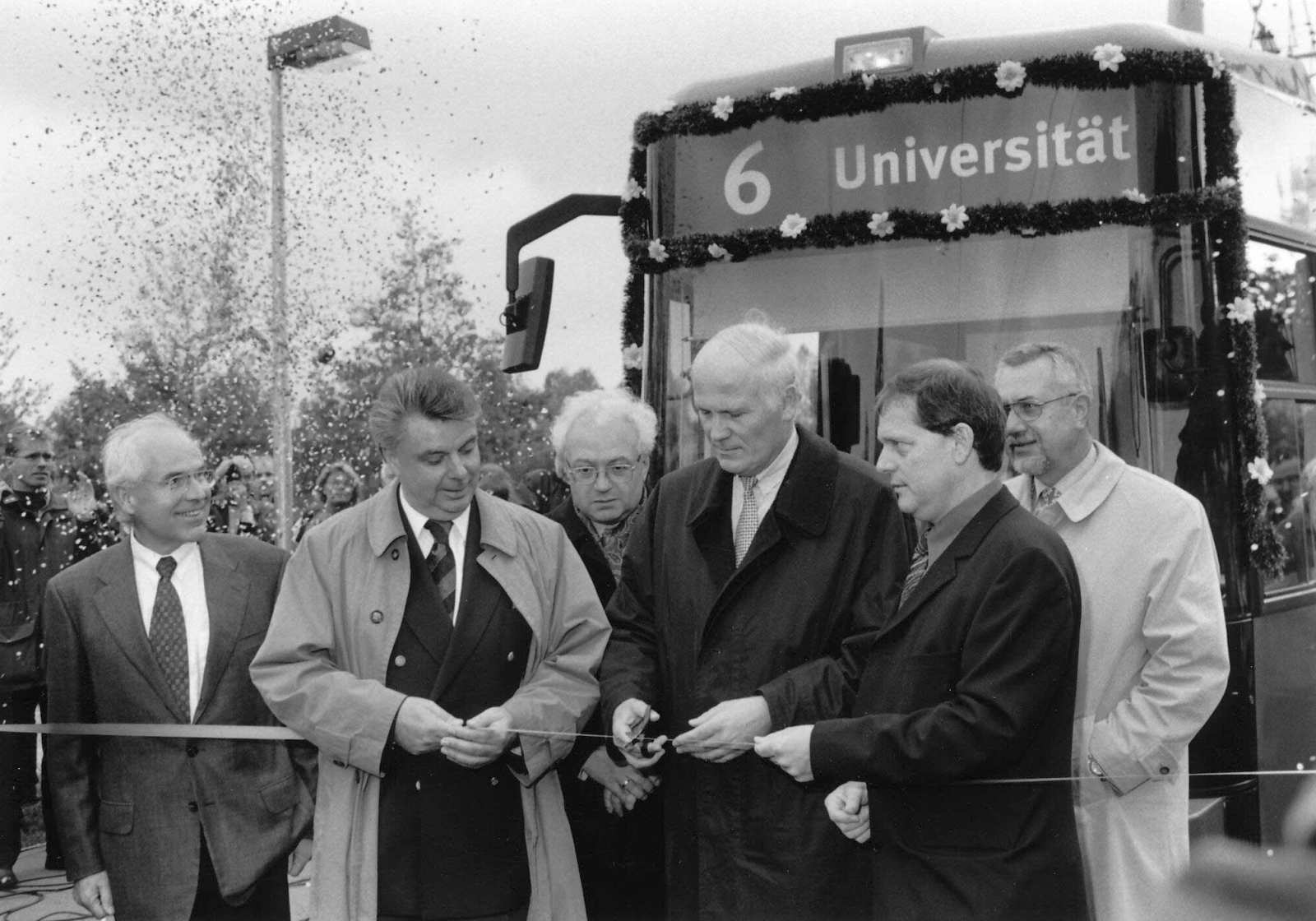 Bausenator Schulte durchtrennt ein Absperrband und gibt damit die neue Linie 6 frei. Neben und hinter ihm stehen mehrere Männer. Außerdem ist dort eine mit Girlanden geschmückte Straßenbahn.