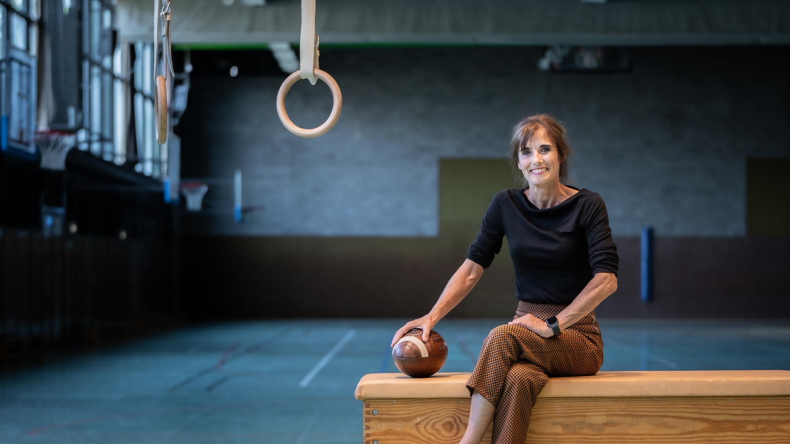 Professorin Ina Hunger sitzt auf einem Kasten in einer Sporthalle.