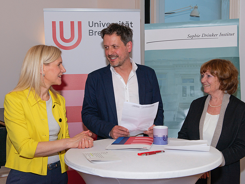 Der Personen stehen um einen Stehtisch.